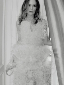 Black and white portrait of a woman wearing a feather-embellished gown holding a small clutch bag indoors.