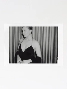 Black and white polaroid photograph of a woman wearing a halter-neck dress against a curtained backdrop.