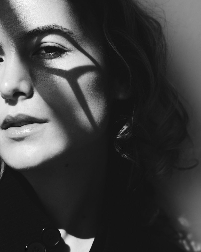 Close-up monochrome portrait of a woman with distinct geometric shadow patterns cast across her face.