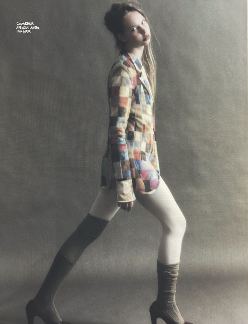 Fashion editorial shot of a young adult female model with blonde hair wearing a multi-colored patchwork blazer with leggings and heeled boots.