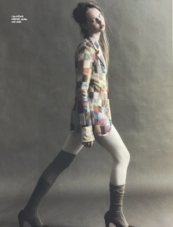 Fashion editorial shot of a young adult female model with blonde hair wearing a multi-colored patchwork blazer with leggings and heeled boots.