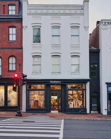 Exterior view of the Huckberry retail storefront featuring large display windows and a multi-story white building facade.