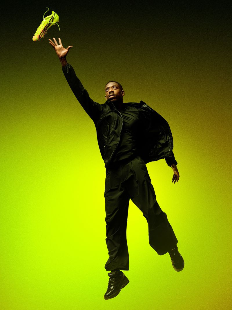 Black man leaping and reaching for a bright yellow soccer cleat against a gradient yellow backdrop for Adidas F50 campaign