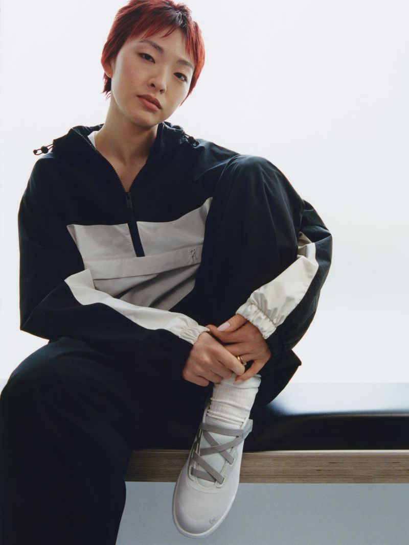 Model with red hair wearing black and white colorblocked activewear sitting on a bench against a plain backdrop.