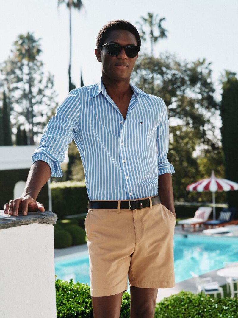 Man wearing a blue striped shirt and khaki shorts by a pool for Tommy Hilfiger