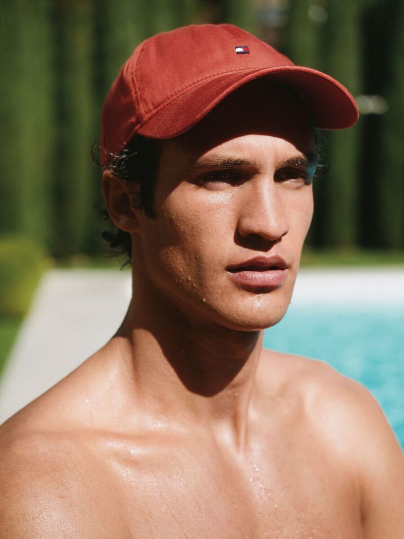 Man wearing a red baseball cap outdoors near a swimming pool for the Tommy Hilfiger SU26 Campaign