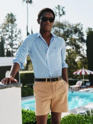 Man wearing a blue striped shirt and khaki shorts by a pool for Tommy Hilfiger