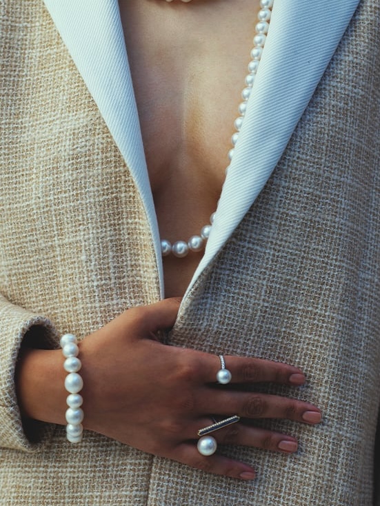 Fashion shot featuring pearls, a blazer, and a hand adorned with pearl rings and a bracelet, highlighting elegant jewelry.
