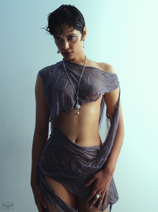Model Zinnia Kumar wearing sheer grey draped apparel with pearl pendant necklace against a plain grey background