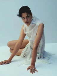 Model Zinnia Kumar crouching on a white surface wearing a textured white dress with fringe details for Russh