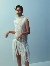 Model Zinnia Kumar wearing a white sheer fringe dress against a light blue studio background for Russh editorial photography.