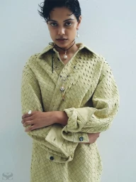 Model Zinnia Kumar wearing a woven sage green shirt and pearl jewellery against a white wall.