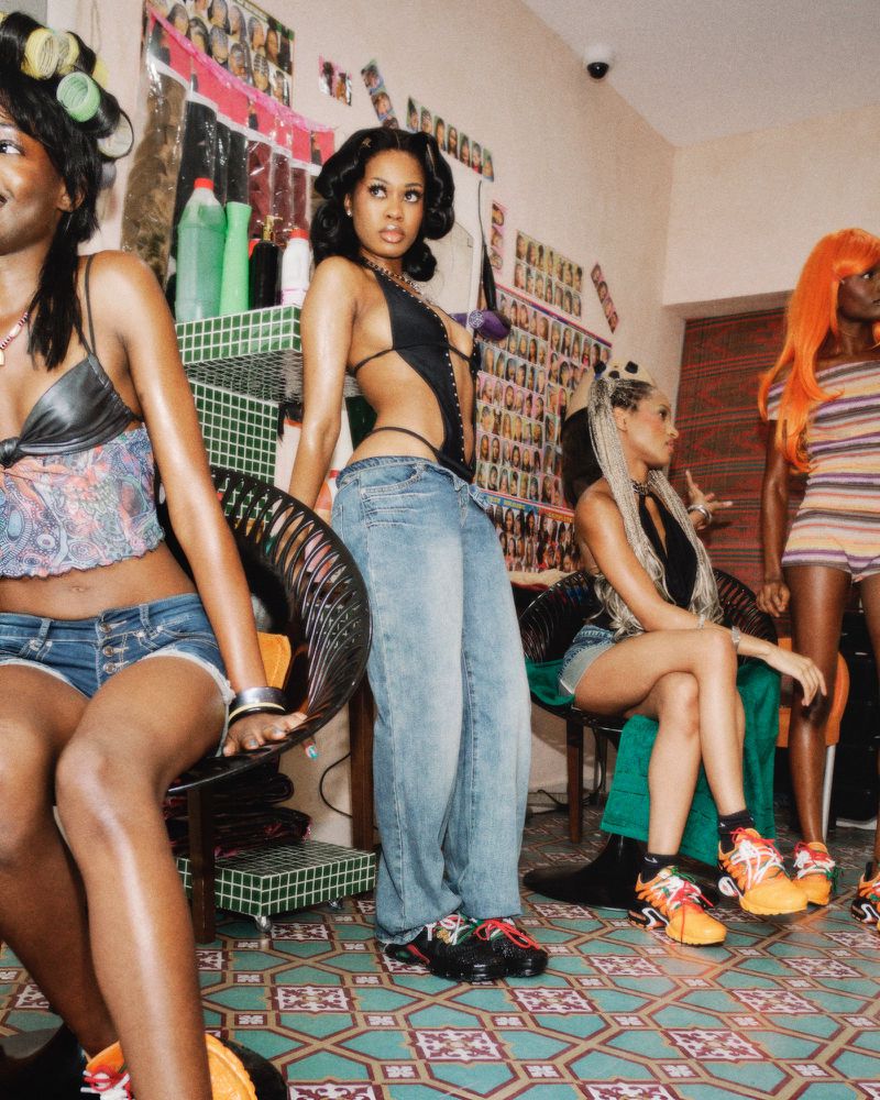 Four Black women in a hair salon setting wearing sneakers and casual attire for Nike campaign by Bolade Banjo.