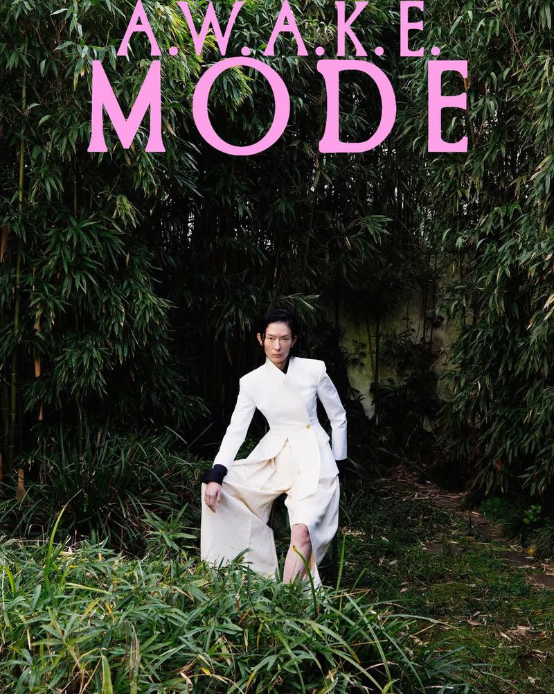 Model in a structured white blazer and wide trousers posing amidst lush green bamboo foliage in an outdoor campaign image.