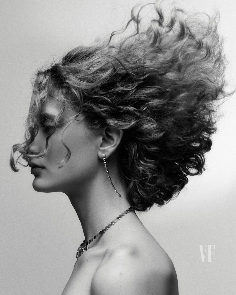 Black and white portrait of a woman in profile with curly hair, wearing jewelry, against a gradient background.