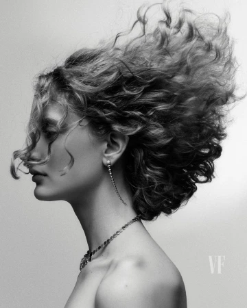 Black and white portrait of a woman in profile with curly hair, wearing jewelry, against a gradient background.
