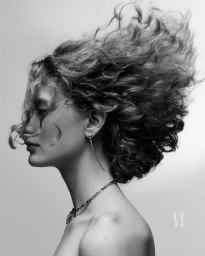 Profile portrait of a woman with curly hair blowing in motion against a plain white background for Vanity Fair Italia