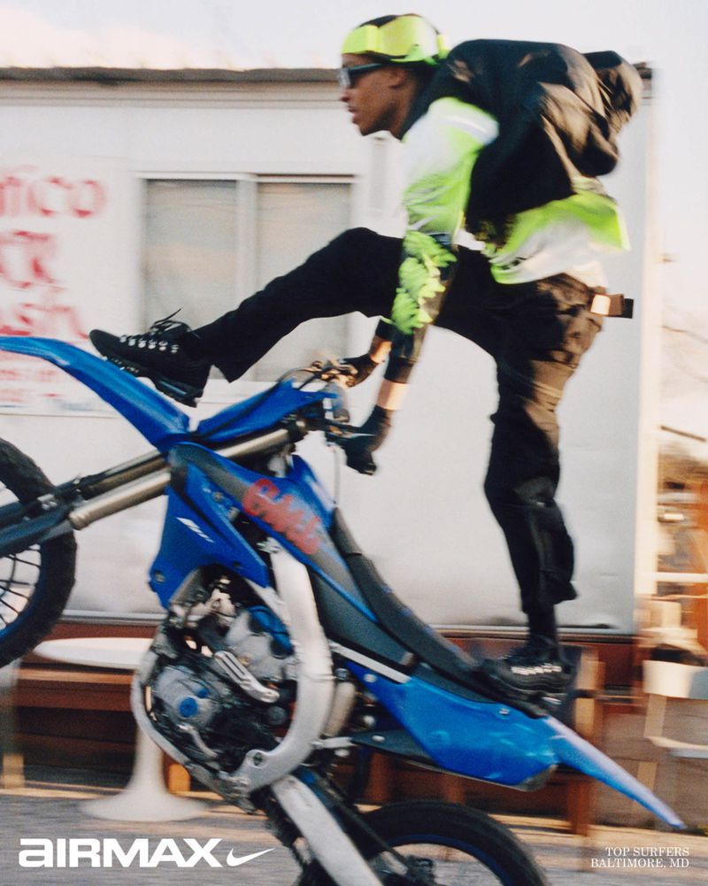 A young man performing a stunt on a blue dirt bike, wearing neon yellow and black apparel, photographed by Bolade Banjo for Nike.