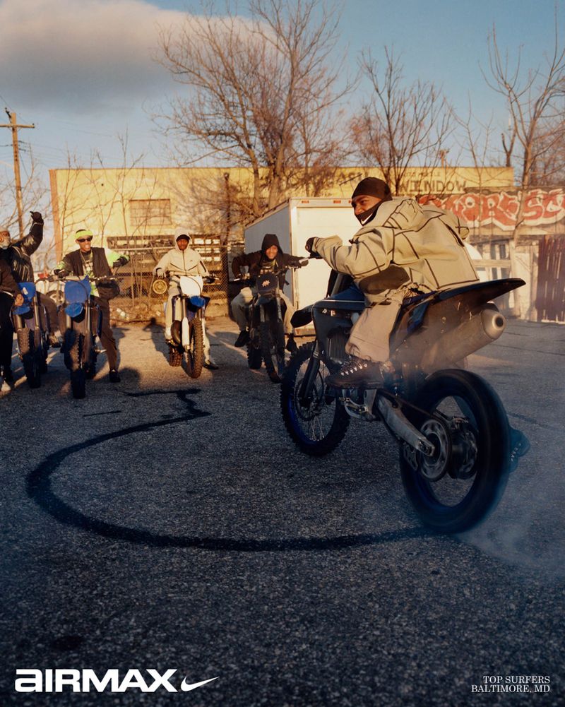 Group of riders on dirt bikes in a paved yard with one rider spinning a tire circle on the ground, captured by Bolade Banjo for Nike.
