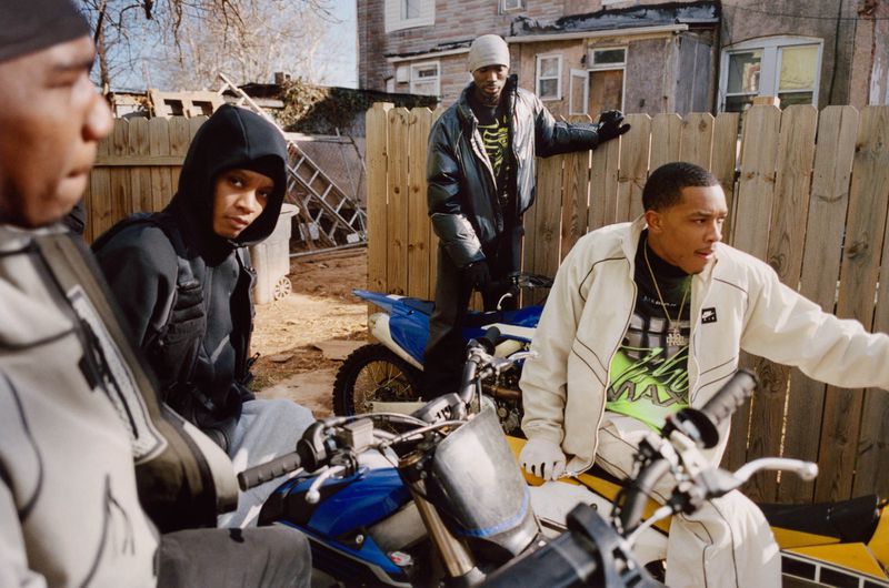 Group of young men posing outdoors near dirt bikes and a wooden fence, captured in a candid documentary style by Bolade Banjo.
