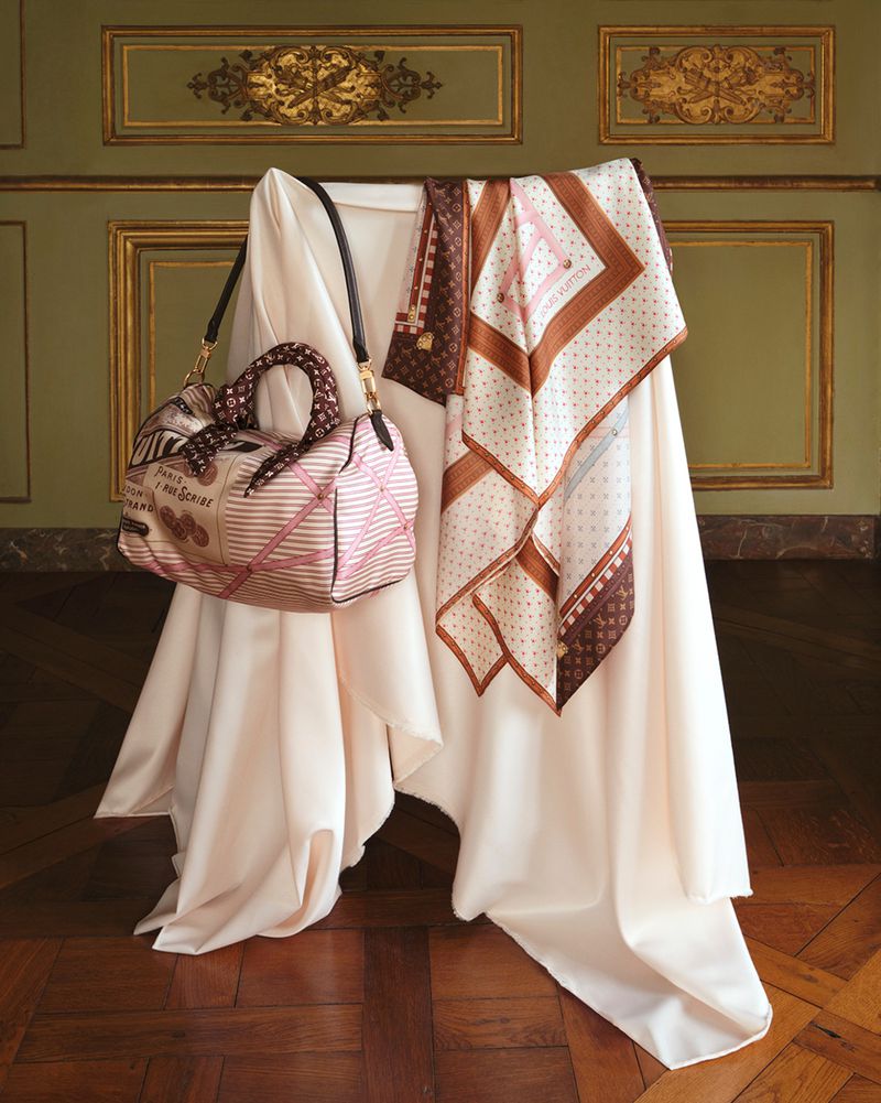 Louis Vuitton handbag and patterned silk scarves displayed on a draped white fabric stand in an ornate room