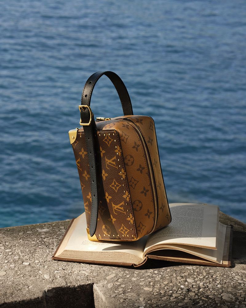Monogram vanity handbag resting on an open book atop stone with ocean view