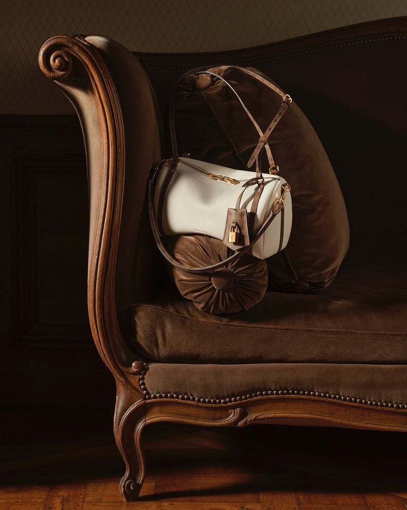 White and brown luxury handbag resting on a dark velvet antique sofa in a warm, dimly lit room.