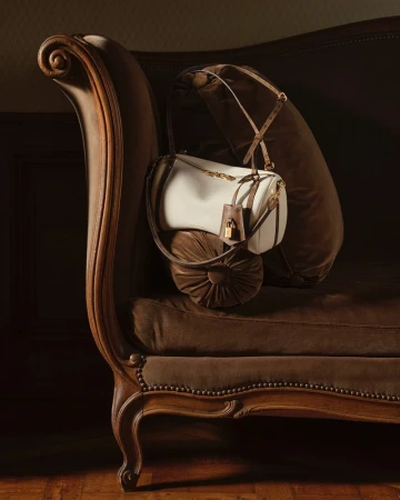 White and brown luxury handbag resting on a dark velvet antique sofa in a warm, dimly lit room.