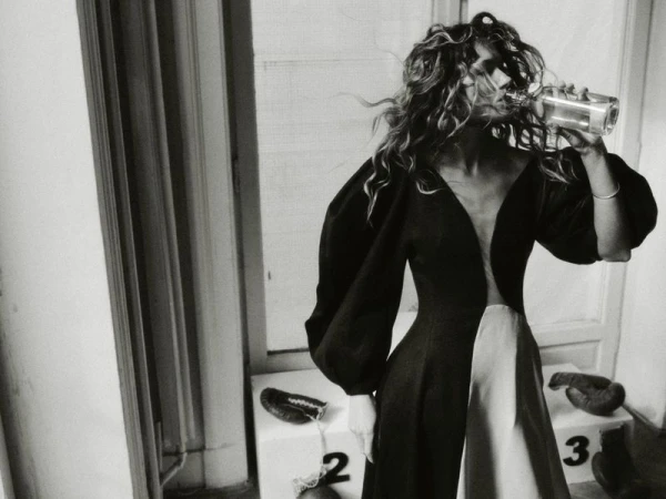 Model drinking from glass bottle wearing a black and white gown with voluminous sleeves for Elle Poland editorial