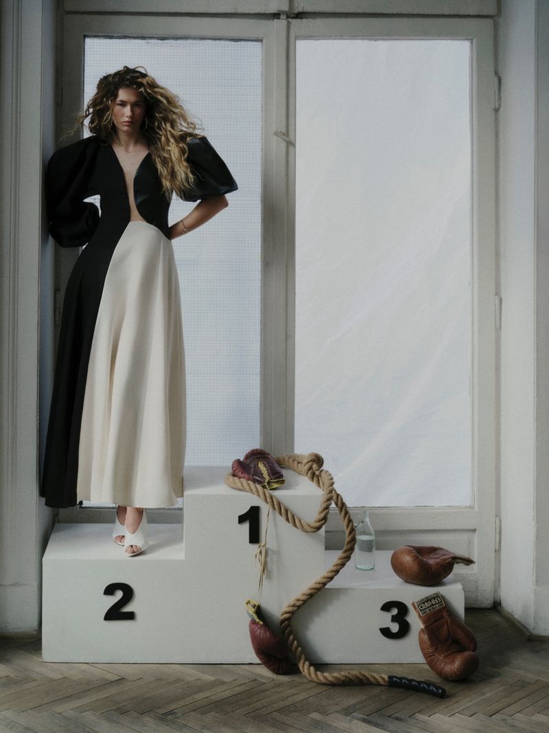 Model standing on a sports podium wearing a black and white dress with oversized sleeves