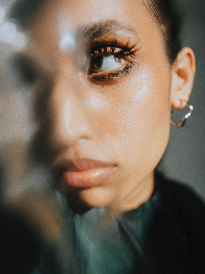 Close-up portrait of an adult female model with long eyelashes and hoop earrings, under soft lighting, showcasing beauty and fashion.