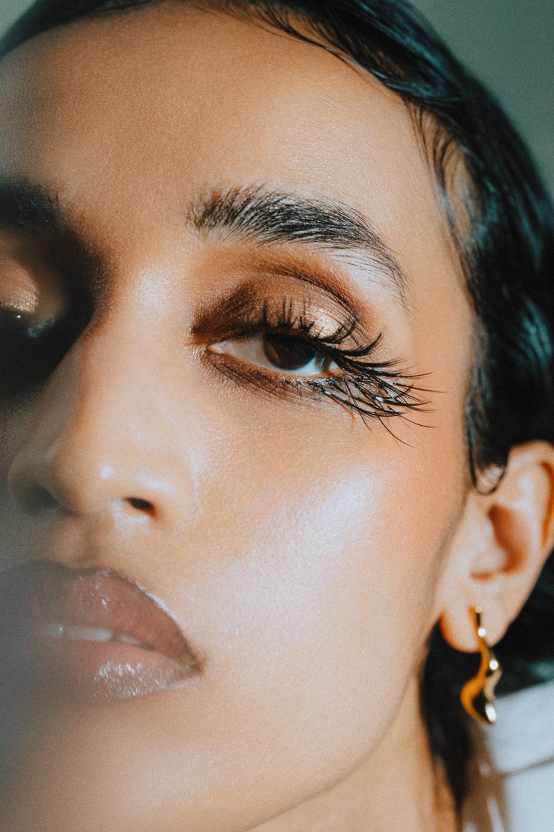 Close-up portrait of a woman with dark hair, glossy lips, glowing skin and long eyelashes wearing an earring with soft lighting.