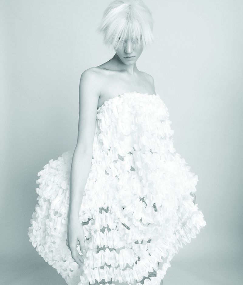 Model with white hair wearing a textured strapless white dress against a pale background