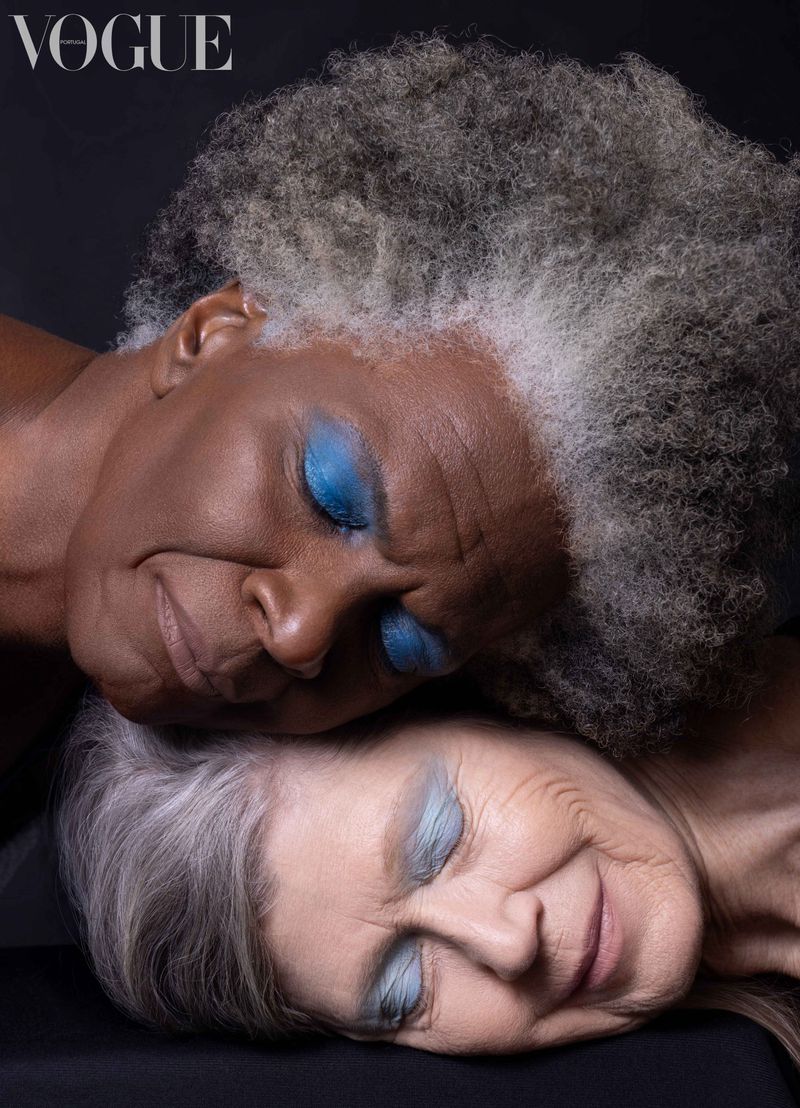 Two elderly women with closed eyes resting together against a dark background featuring Vogue Philippines branding in the corner