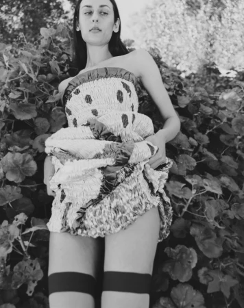 Black and white editorial portrait of a model in a patterned strapless dress posing amongst dense foliage.