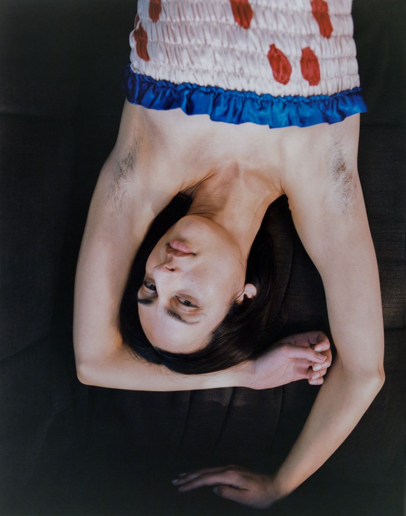 Model lying upside down wearing a patterned strapless top with a blue trim, arms raised against a dark background