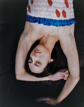 Model lying upside down wearing a patterned strapless top with a blue trim, arms raised against a dark background