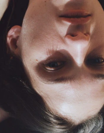Close-up portrait of a model with dark hair under warm directional light casting stark shadows across her face.