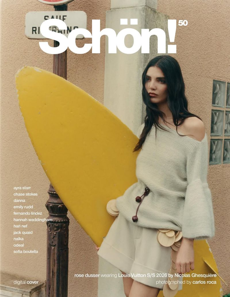 Woman holding large yellow surfboard standing on a street next to a sign for Schön Magazine cover