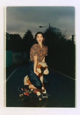 Woman riding a toy rocking horse mounted on a skateboard outdoors on an asphalt road during twilight.