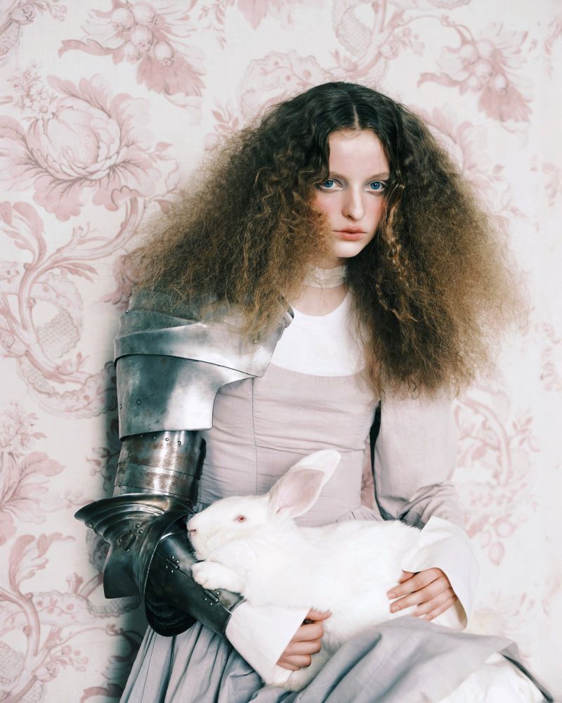 Model with voluminous curly hair wearing steel plate armour on one arm while holding a white rabbit for Vogue Portugal