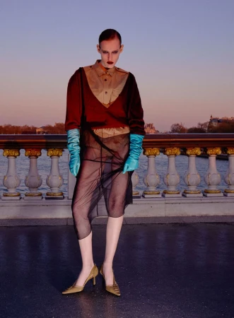 Model in red sweater and sheer skirt wearing bright blue gloves on a bridge at dusk for V Magazine China editorial