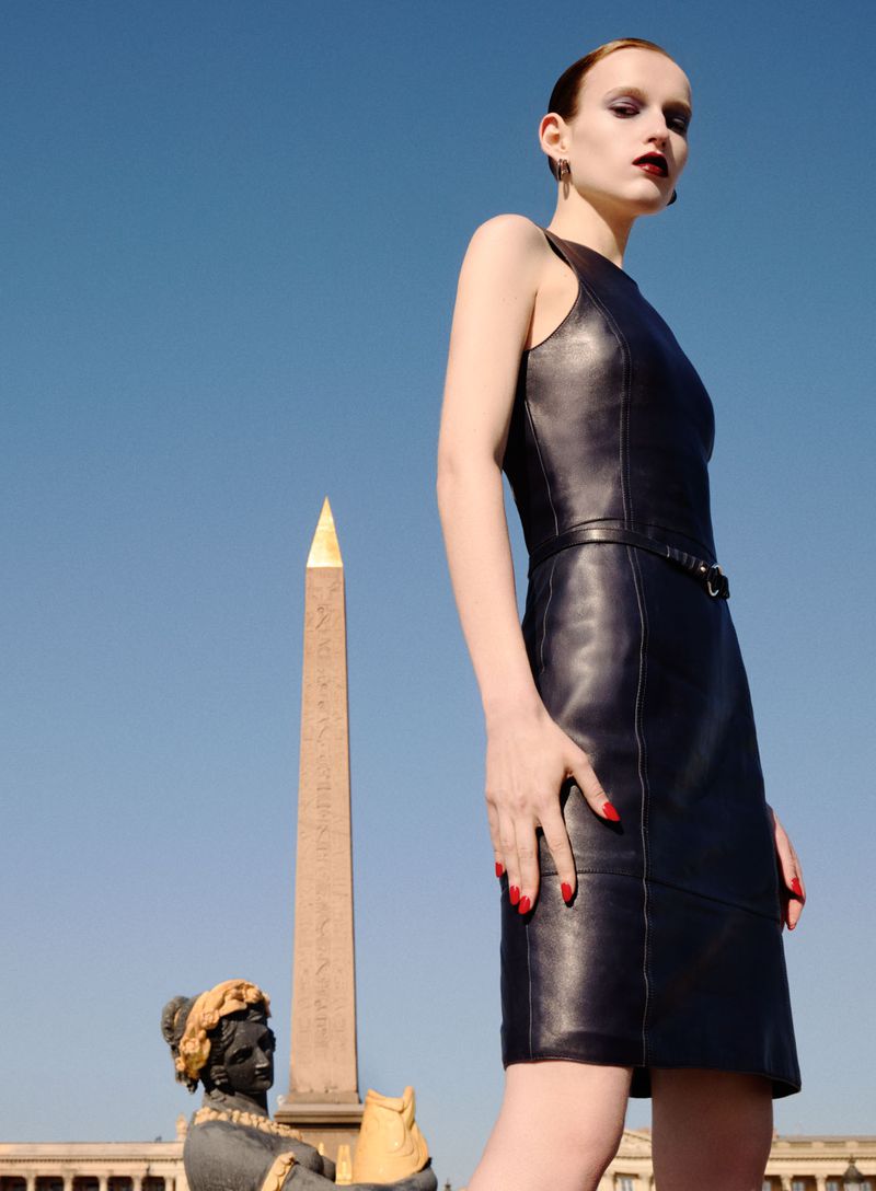 Model in a black leather dress standing against a clear blue sky with an obelisk monument visible below