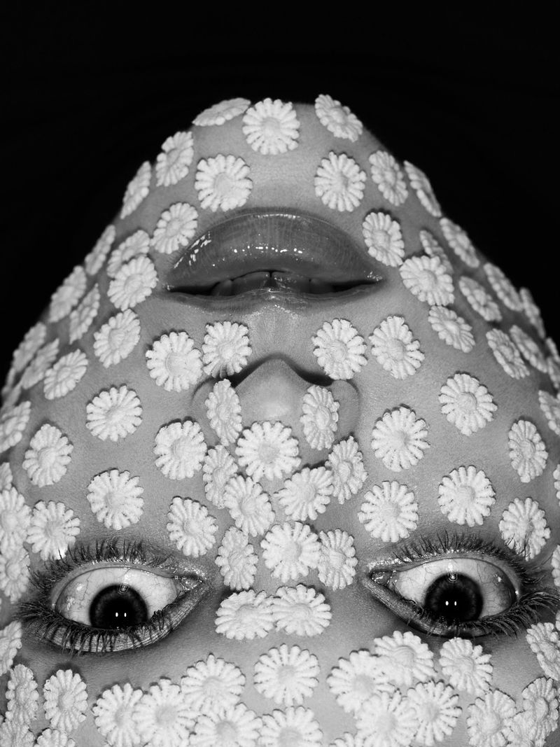 Close-up portrait of model Gertrud Rose covered entirely in small white daisy flowers photographed by Willy Vanderperre.