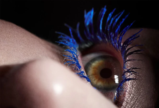 Extreme close-up of a human eye with vibrant blue eyelashes and detailed iris in a dark setting
