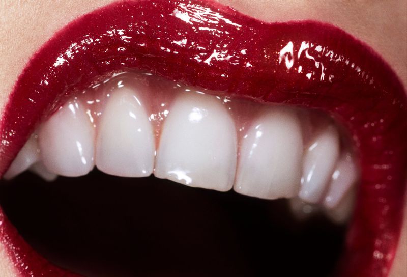 Close-up macro shot of parted lips wearing glossy dark red lipstick revealing white teeth for Beyond Noise issue 5 by Willy Vanderperre.
