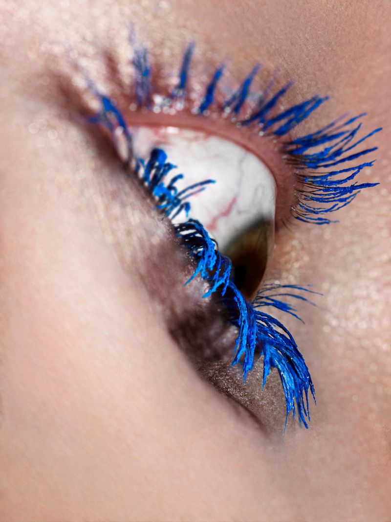 Extreme close-up macro view of a human eye featuring vibrant blue mascara on long eyelashes and soft shimmering eyeshadow.