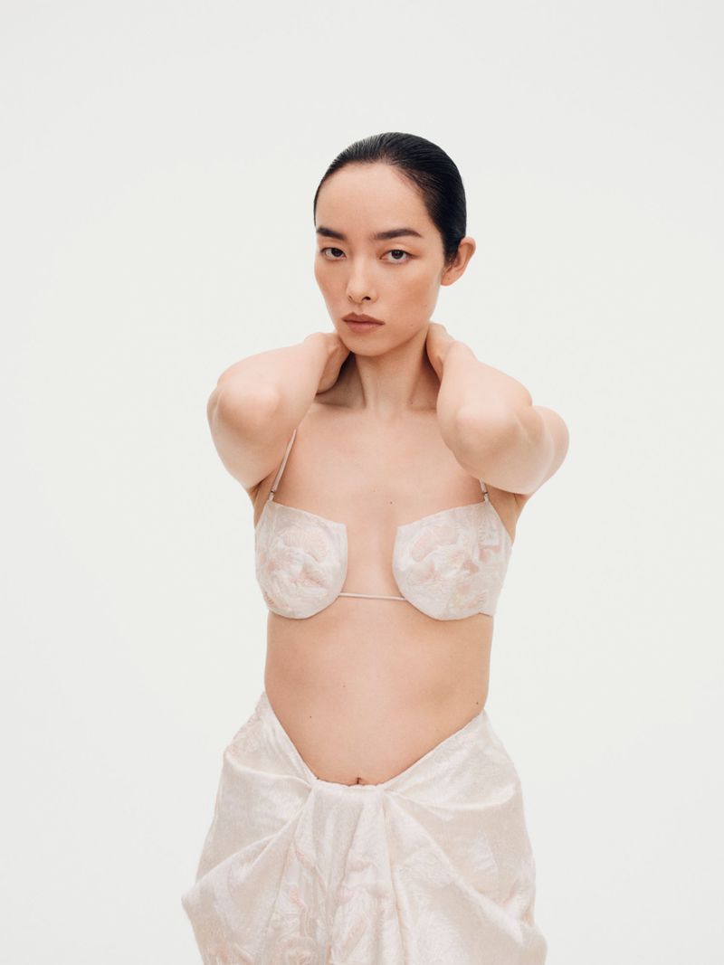 Model FeiFei Sun posing against a plain white seamless studio background wearing light-colored textured garments.