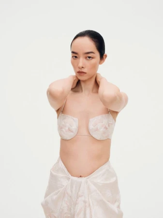 Model FeiFei Sun posing against a plain white seamless studio background wearing light-colored textured garments.