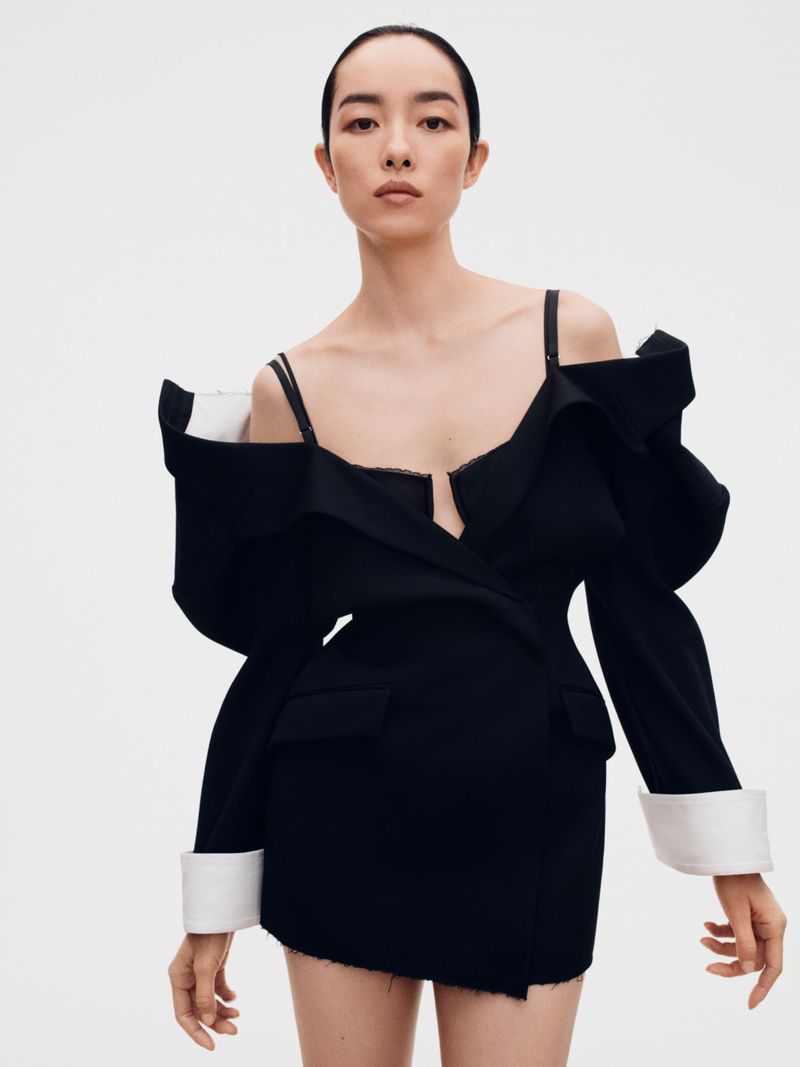 Model FeiFei Sun wearing a structured black dress with white cuffs against a white seamless background